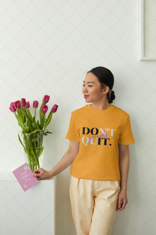 Person wearing a yellow t-shirt with 'DON'T QUIT' text, holding flowers and a card.